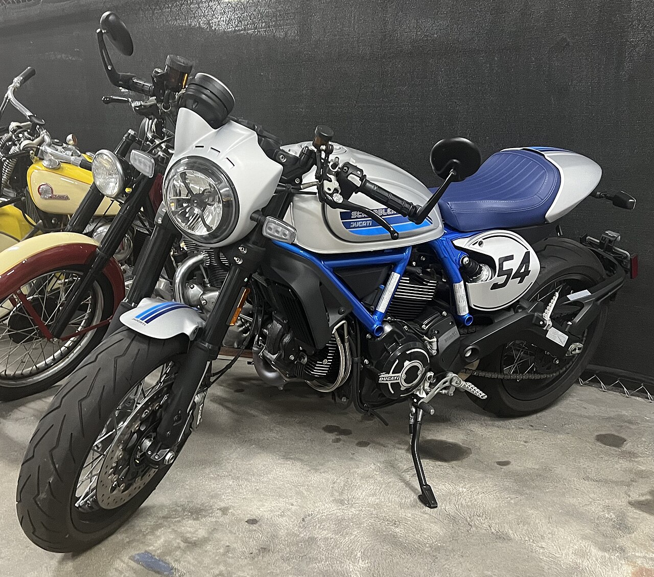 Silver and blue Ducati Scrambler Cafe Racer with a blue seat and number 54 side panel at the Petersen Automotive Museum