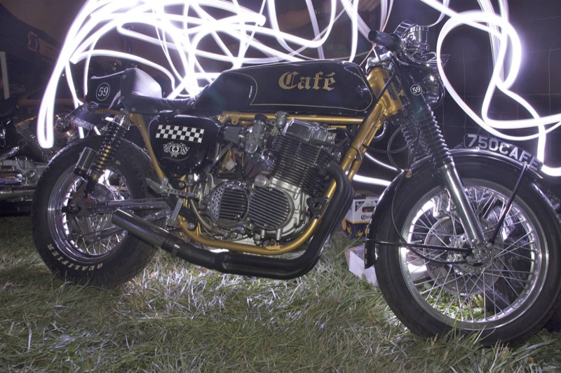 Honda CB750 cafe racer with a gold frame, black tank and number 59 tail, photographed at night