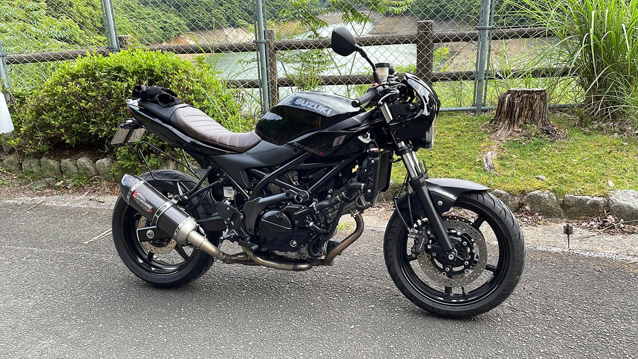 Black Suzuki SV650X with low handlebars, a ribbed seat, headlight cowl and aftermarket Yoshimura exhaust, parked outdoors