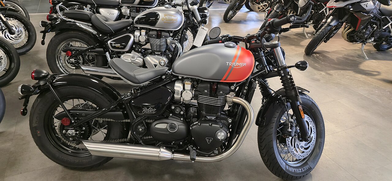 Gray and red Triumph Bonneville Bobber with a solo seat, shown from the right side in a showroom