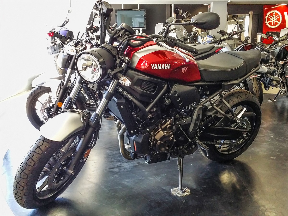 Red and silver Yamaha XSR700 with round earlier-style headlight, upright bars and a two-person seat, photographed indoors in August 2018